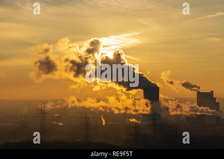 Dampf steigt aus einem Schornstein auf eine Fabrik gegen das Sonnenlicht goldenen Stunde Silhouette Stockfoto