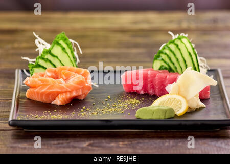 Rot und Orange in Scheiben Fischfilet und Beilage. Lachs, Thunfisch, Gurkenscheiben, weißer Ingwer, Wasabi und Zitrone. Stockfoto