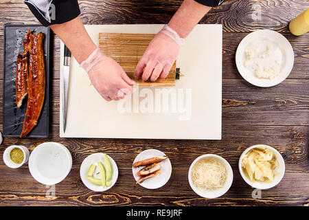 Hände Rolling Sushi in Bambus Matte. Prozess der Faltung in Bambus sushi Matte, Ansicht von oben. Stockfoto