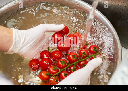 Koch Cherry Tomaten Eintauchen in Wasser. Tomaten in Metall Schüssel voll Wasser sinkt. Stockfoto