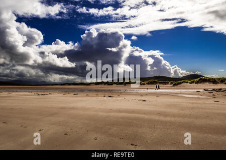 Paar mit Hund bei einem Spaziergang auf dem sandigen Achnahaird Beach in Schottland Stockfoto