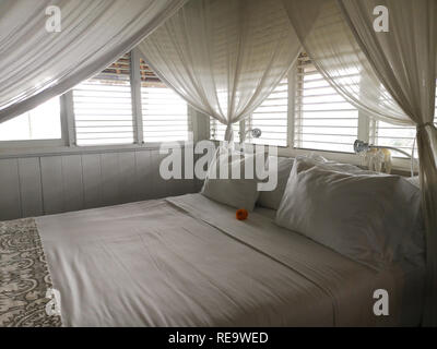 Kissen auf einem weißen Himmelbett mit Vorhängen, Licht aus den Fenstern kommen Stockfoto