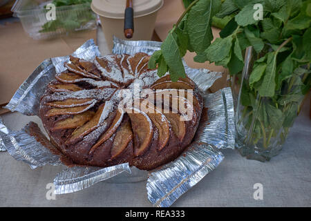 Frische heiße hausgemachte gebackene Apfelkuchen auf einem Tisch in der Nähe frische grüne Blätter. Makro Stockfoto