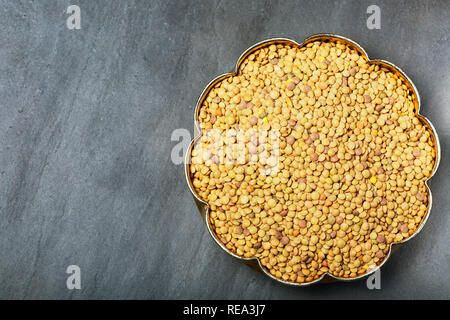 Roh Linsen in einem goldenen Kupfer Schale auf Schwarz Stein Hintergrund. Gesunde vegetarische Essen Konzept. Superfoods. Ansicht von oben, kopieren. Linsen sind reich an Stockfoto