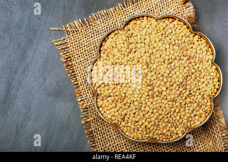 Roh Linsen in einem goldenen Kupfer Schale auf Schwarz Stein Hintergrund. Gesunde vegetarische Essen Konzept. Superfoods. Ansicht von oben, kopieren. Linsen sind reich an Stockfoto