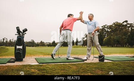 Ältere Golfspieler hoch fünf auf die Driving Range. Zwei reife Golf Spieler geben einen hohen fünf nach einem erfolgreichen Training auf die Strecke fahren. Stockfoto