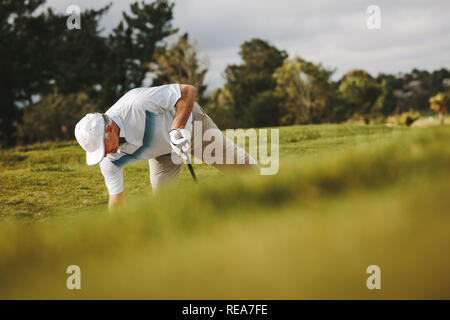 Ältere Golfspieler den Ball auf dem Sand Bunker für seinen Schuss. Pro Golfspieler spielen auf dem Golfplatz. Stockfoto