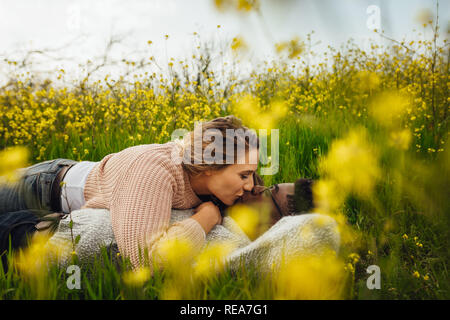Romantische interracial Paare liegen im grünen Gras und Küssen. Paar küssen Auf blühende Wiese im Freien. Stockfoto