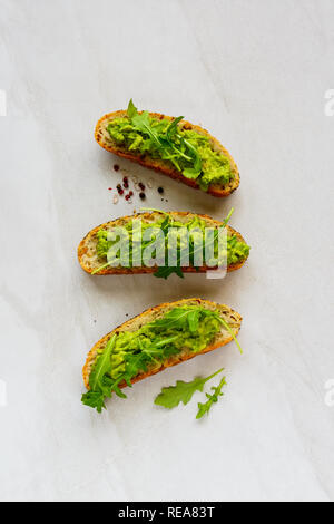 Drei avocado Toasts mit Rucola flach. Gute Fette raw Gesunde Ernährung Konzept. Stockfoto