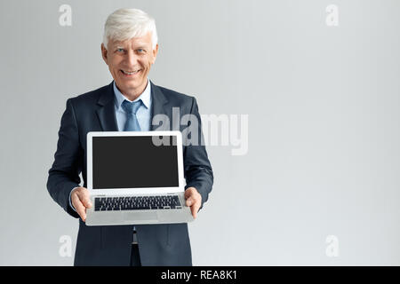 Business Lifestyle. Unternehmer stehen isoliert auf grau angezeigt Bildschirm des Laptop lächelt Fröhlich Stockfoto