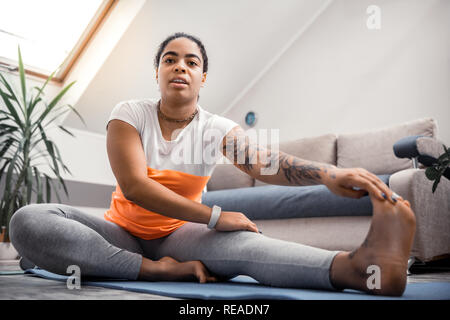 Übergewicht dunkelhäutige Dame mit Tattoos ihr Bein berühren. Stockfoto