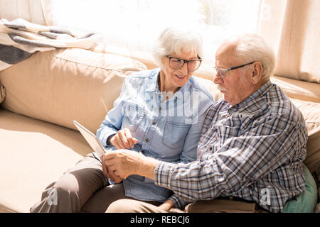 Portrait des modernen senior Paar mit digitalen Tablet sitzen auf der Couch zu Hause im Sonnenlicht Platz kopieren Stockfoto