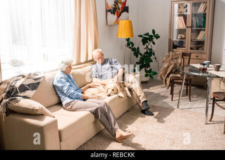 Volle Länge Portrait von Happy senior Paar Kuscheln mit Hund sitzt auf der Couch im Sonnenlicht, kopieren Raum Stockfoto