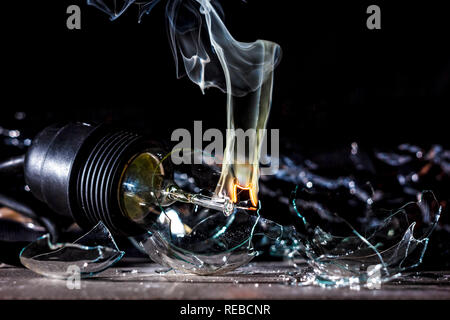 Erstaunliche Explosion einer brennenden Lampe mit Splitter und Rauch auf einem schwarzen Hintergrund mit einem Flash Stockfoto