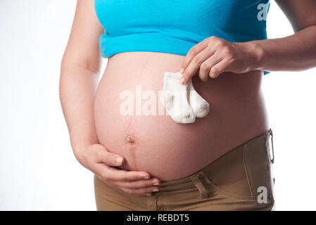 Schwangere Frau halten Baby Socken auf weißem Hintergrund Stockfoto