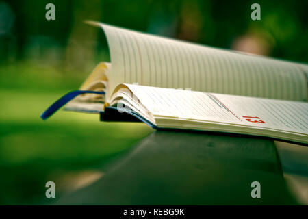 Freitag 13, Wind dreht die Seiten von Open Notebook liegt auf hölzernen Handlauf in Park, Geschäftskonzept. Stockfoto