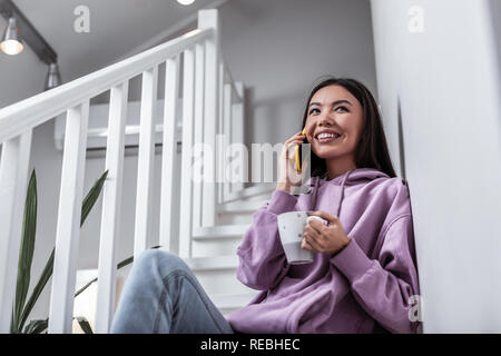 Fröhliche junge Frau, die ihrem Freund anrufen kann, während sie Tee trinken. Stockfoto