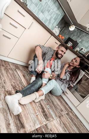 Der bärtige Mann mit squared Shirt seine Frau in der Küche verbinden Stockfoto