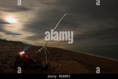 Eine lange Exposition von einem Angler in der Nacht mit einem Scheinwerfer Angeln am Chesil Beach in Dorset. Andere Angler können im Hintergrund gesehen werden. Die super Blut Stockfoto