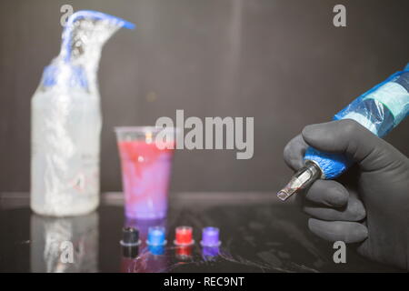 Tattoo artist Holding ein Tattoo Maschine zur Hand und Tattoo Tinte in die Kappen auf die Tabelle in Tattoo Studio. Stockfoto