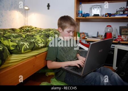 Junge, 11, Arbeiten mit seinem Computer zu Hause in seinem Schlafzimmer tun Schule Hausaufgaben Stockfoto