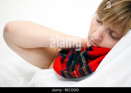 Eine junge Frau mit Halsschmerzen und Erkältung im Bett, mit einem Schal Stockfoto