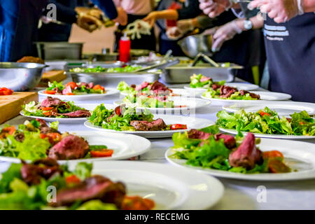 Warmes Roast Beef, frischer Salat und Tomaten serviert auf Weiße Platten. Kochen Master Class, Workshop mit Menschen lernen, wie man zu Kochen rund um den Tisch Stockfoto