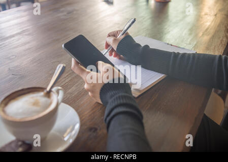 Frau hand mit Smartphone und Verfassen von Notizen Stockfoto