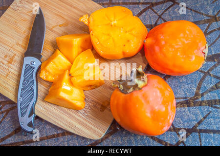 Blick von oben auf eine Kaki Obst auf einem hacken Platte geschnitten. Andere Früchte sind Tabelle gehalten Stockfoto