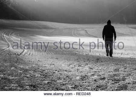 Ein Mann in einer Jacke und Kappe Überqueren einer Frost bedeckt Feld in Bayern an einem Winter. Stockfoto