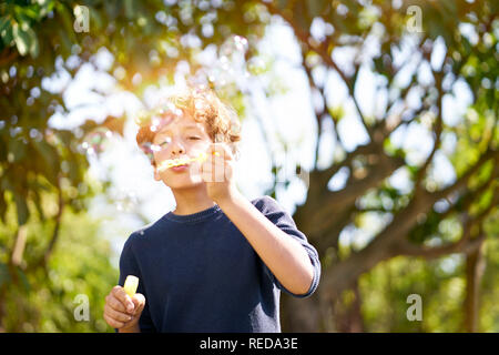 10-jährige italienische Junge bläst Seifenblasen draußen im Park. Stockfoto