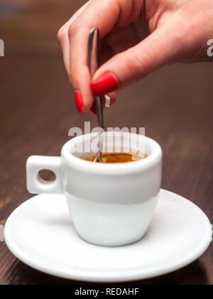 In der Nähe der weiblichen Hand mit Tasse Espresso und Löffel. Stockfoto