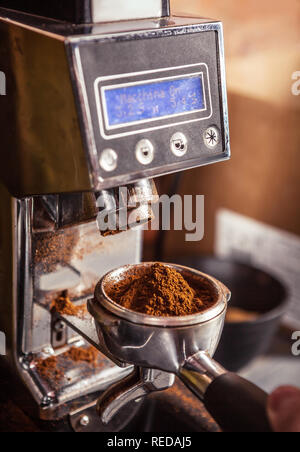 Zugeschnittenes Bild von Barista mit kaffeemühle Holding portafilter mit gemahlenen Kaffee. Stockfoto