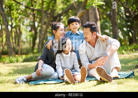 Asiatische Familie mit zwei Kindern Spaß sitzen auf Gras sprechen plaudernd im Freien in Park Stockfoto