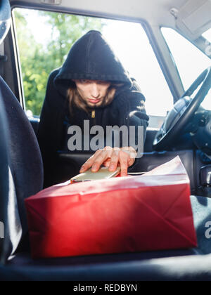 Anti Theft system problem Konzept. Einbrecher, Dieb Mann mit schwarzer Kleidung in Auto, Diebstahl von Smartphone und Rot Warenkorb Stockfoto