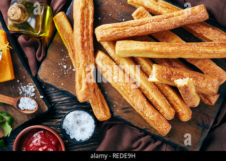 Ansicht von oben von Käse Strohhalme, kitschigen Brot klebt auf einem Holzbrett mit Geriebener Cheddar-Käse, Tomatenmark, Olivenöl auf eine Tabelle, Ansicht her Stockfoto