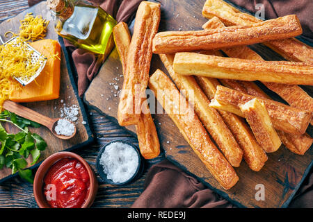 Ansicht von oben von Käse Strohhalme, kitschigen Brot klebt auf einem Holzbrett mit Geriebener Cheddar-Käse, Tomatenmark, Olivenöl auf eine Tabelle, Ansicht her Stockfoto