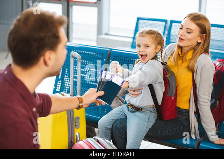 Selektiver Fokus der aufgeregten Tochter lächelnd mit Mutter in der Nähe von Vater mit Pässen mit Flugtickets Stockfoto