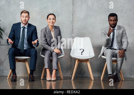 Multiethnischen Geschäftsleute sitzen in der Nähe der Karte mit Fragezeichen auf Stuhl in der Wartehalle und Kamera Stockfoto