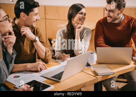 Lächelnd Gruppe von Kollegen sprechen in Cafe in der Nähe von Laptops Stockfoto