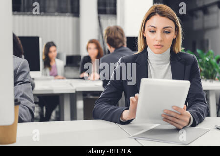 Junge Geschäftsfrau mit digitalen Tablet während der Arbeit mit den Kollegen im Open Space Office konzentriert Stockfoto