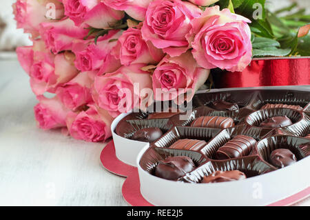 Dutzend rosa Rosen mit einem herzförmige Schachtel Schokolade Süßigkeiten für Valentinstag über eine Holz Hintergrund. Stockfoto