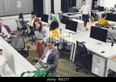 Hohe Betrachtungswinkel der Jungen multiethnischen Geschäftsleute arbeiten mit digitalen Geräten in Open Space Office Stockfoto