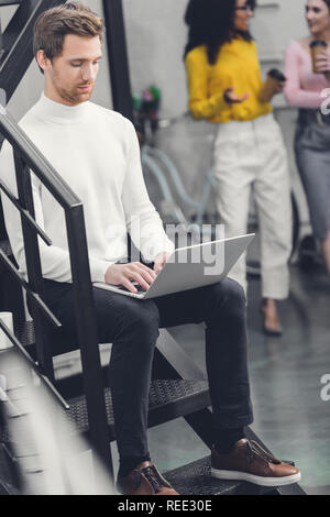 Junger Mann sitzt im Treppenhaus und mit Laptop im Büro ausgerichtet Stockfoto