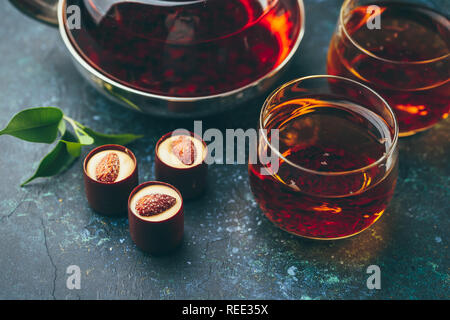 Zwei Glas Tassen und Teekanne mit schwarzem Tee und Pralinen auf dunklem Hintergrund. Stockfoto