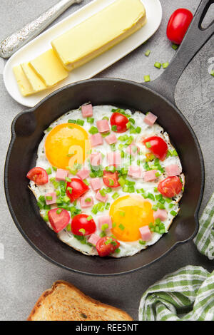 Spiegeleier in Schwarz pan mit Schinken, Tomaten und Frühlingszwiebeln. Köstliches Frühstück mit Toast und Butter. Die klassische Englische Stockfoto