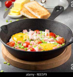 Spiegeleier in Schwarz pan mit Schinken, Tomaten und Frühlingszwiebeln. Köstliches Frühstück mit Toast und Butter. Die klassische Englische Stockfoto