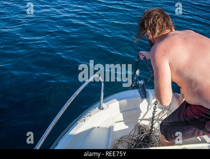 Ein junger Mann auf einem Boot Ziehen am Seil eines Ankers Stockfoto
