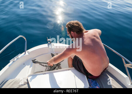 Ein junger Mann auf einem Boot Ziehen am Seil eines Ankers Stockfoto