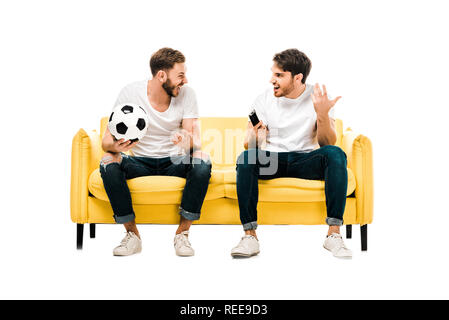 Glückliche junge Männer, die mit Fußball und Fernbedienung an einander Suchen isoliert auf weißem Stockfoto